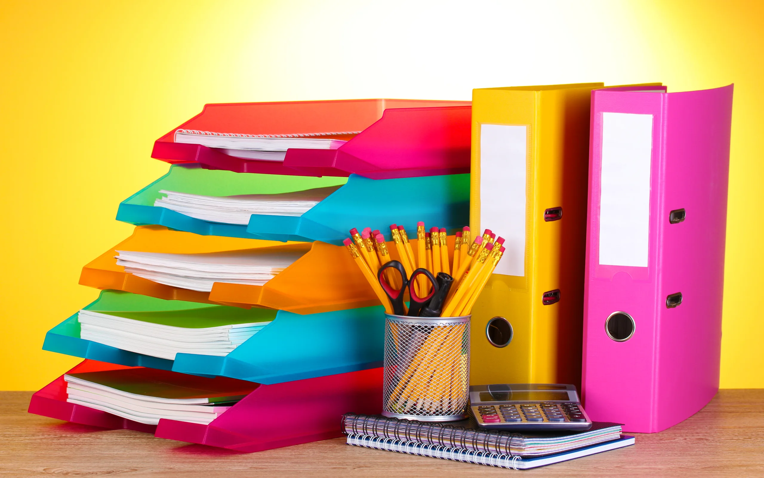bright paper trays and stationery on wooden table on yellow background